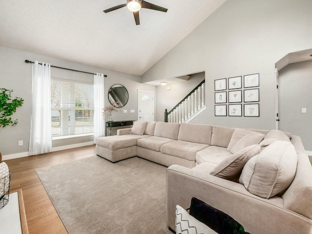 living room featuring high vaulted ceiling, a ceiling fan, wood finished floors, baseboards, and stairs