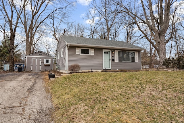 view of front of house with a storage unit, an outbuilding, a front lawn, aphalt driveway, and roof with shingles