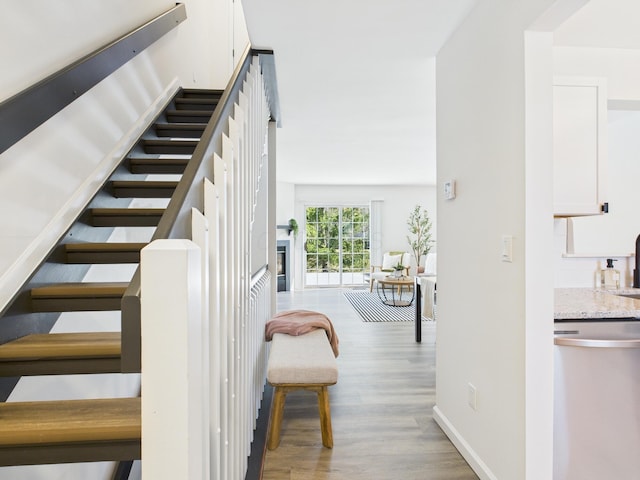 stairway with a glass covered fireplace, wood finished floors, and baseboards