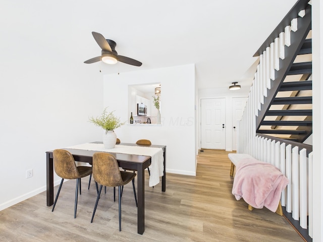 dining space featuring stairway, baseboards, a ceiling fan, and light wood finished floors