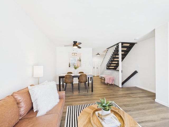 living area featuring stairway, baseboards, light wood-type flooring, and ceiling fan