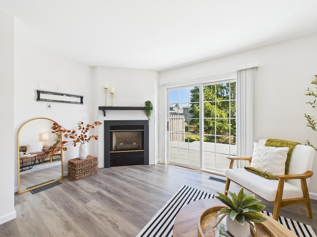 sitting room featuring a glass covered fireplace, baseboards, visible vents, and wood finished floors