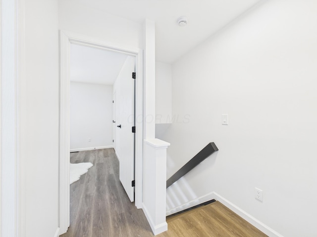 hall with an upstairs landing, baseboards, and wood finished floors