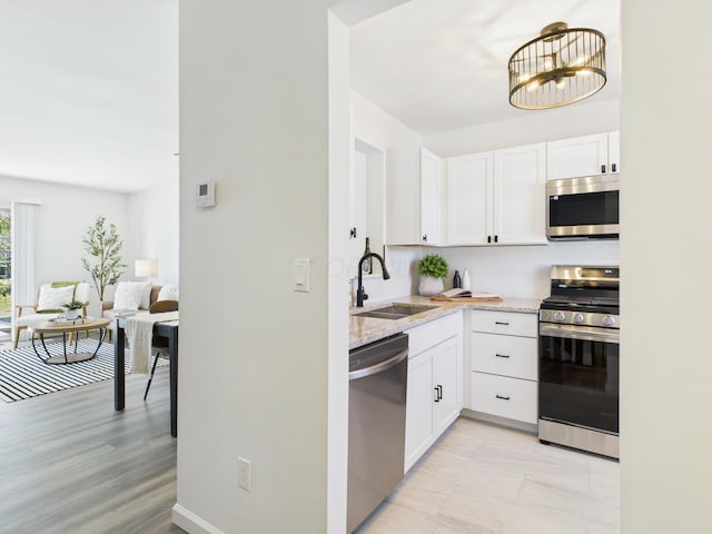 kitchen with light stone counters, a sink, appliances with stainless steel finishes, white cabinetry, and tasteful backsplash