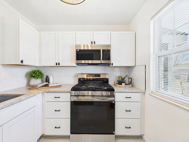 kitchen with backsplash, plenty of natural light, white cabinetry, and appliances with stainless steel finishes