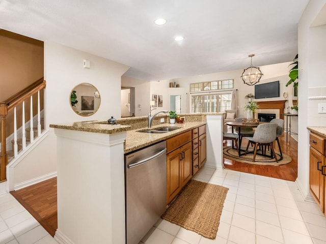 kitchen with an island with sink, light stone counters, brown cabinets, stainless steel dishwasher, and a sink