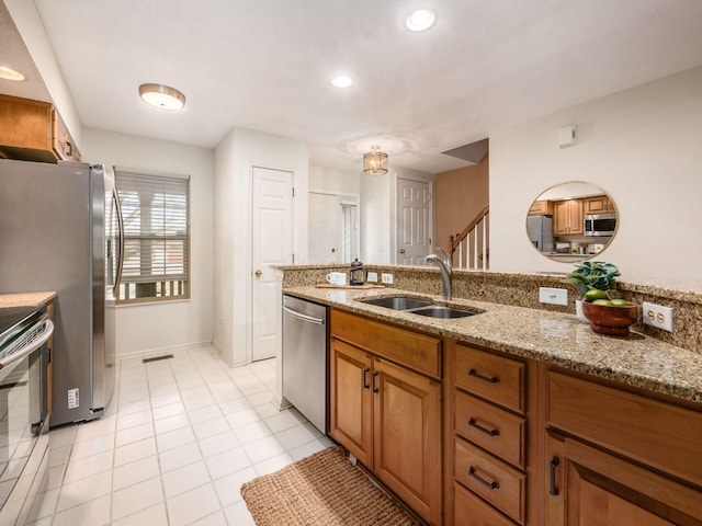 kitchen with light tile patterned floors, light stone countertops, stainless steel appliances, a sink, and brown cabinets