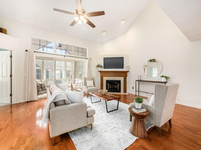 living area with a fireplace with flush hearth, wood finished floors, and high vaulted ceiling