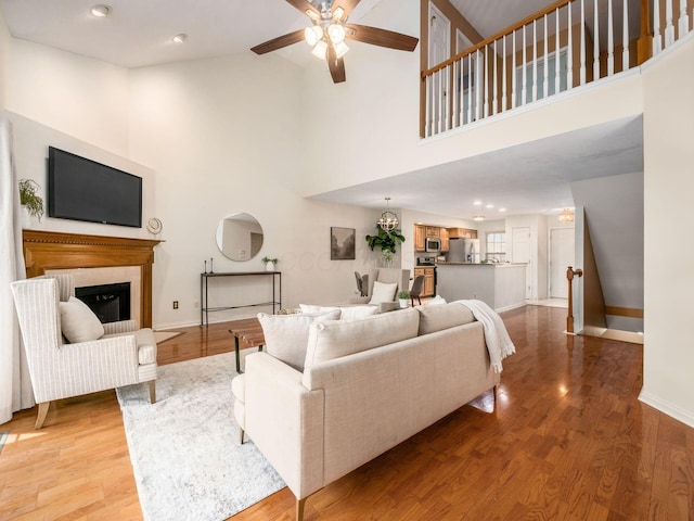 living room with a glass covered fireplace, wood finished floors, a high ceiling, baseboards, and ceiling fan