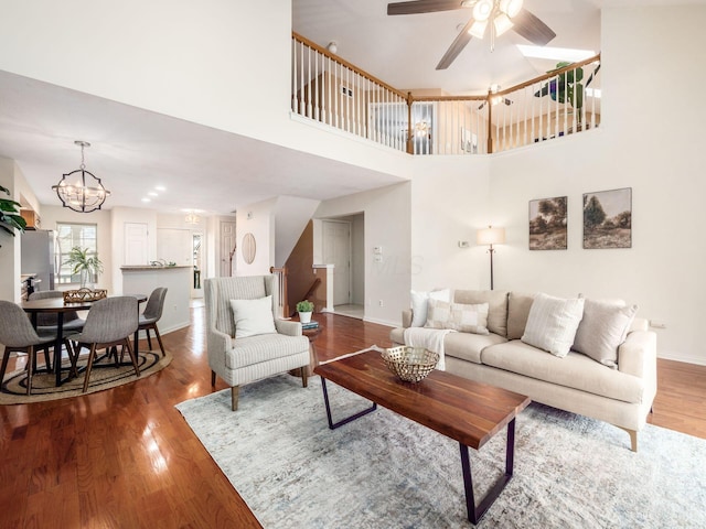 living room featuring baseboards, a high ceiling, wood finished floors, and ceiling fan with notable chandelier