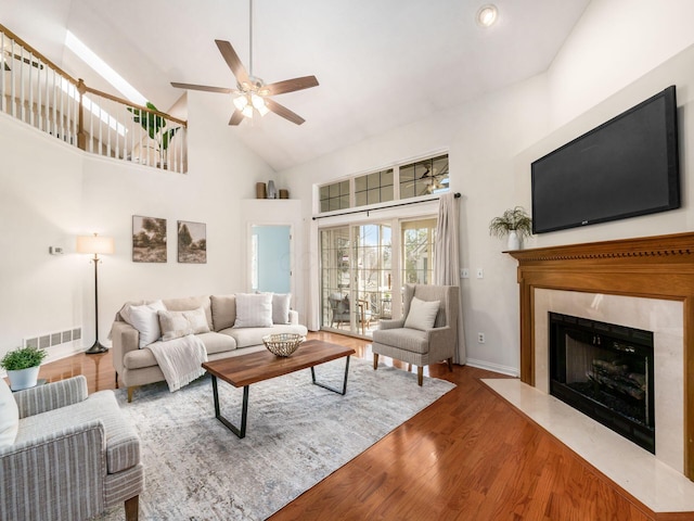 living room featuring visible vents, high vaulted ceiling, wood finished floors, a high end fireplace, and baseboards