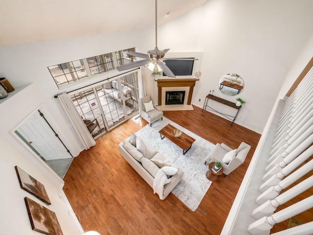 living room featuring a fireplace with raised hearth, high vaulted ceiling, a ceiling fan, and wood finished floors