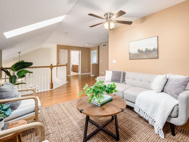 living room featuring ceiling fan, baseboards, lofted ceiling with skylight, and wood finished floors