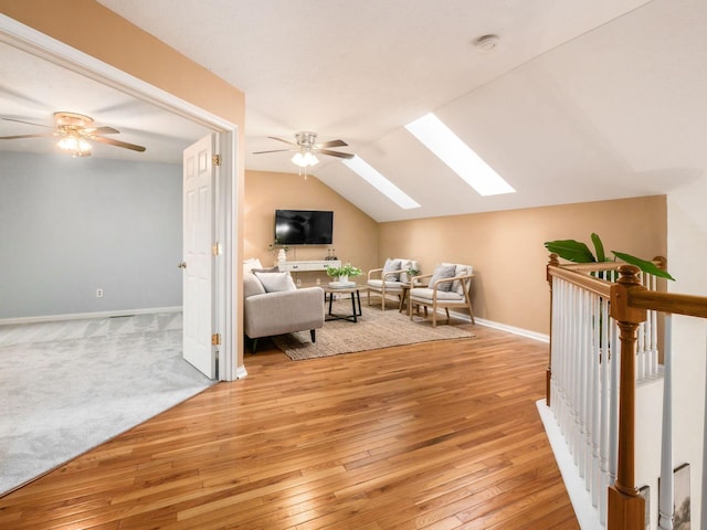 living area with baseboards, vaulted ceiling with skylight, light wood-style flooring, and a ceiling fan