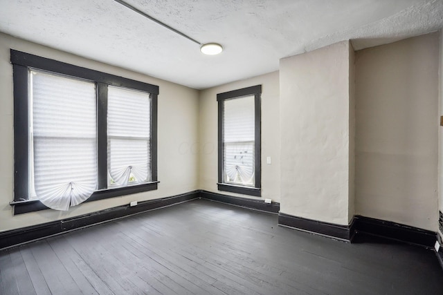 empty room featuring a textured ceiling, baseboards, and wood-type flooring