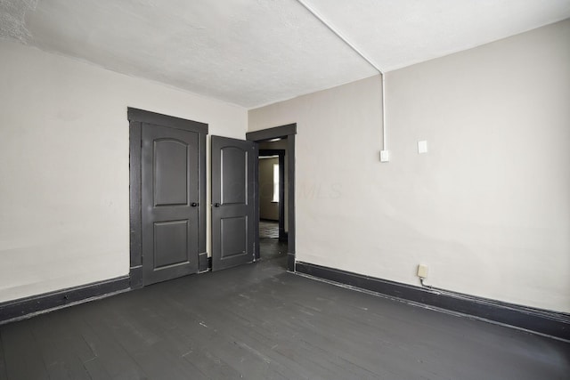 spare room featuring baseboards and dark wood-style flooring