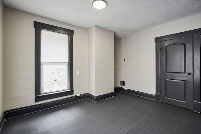 unfurnished room with visible vents, baseboards, and dark wood-style flooring