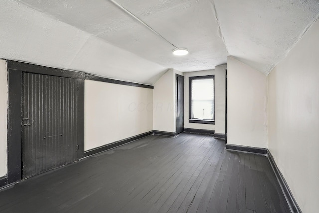 bonus room with dark wood finished floors, vaulted ceiling, baseboards, and a textured ceiling