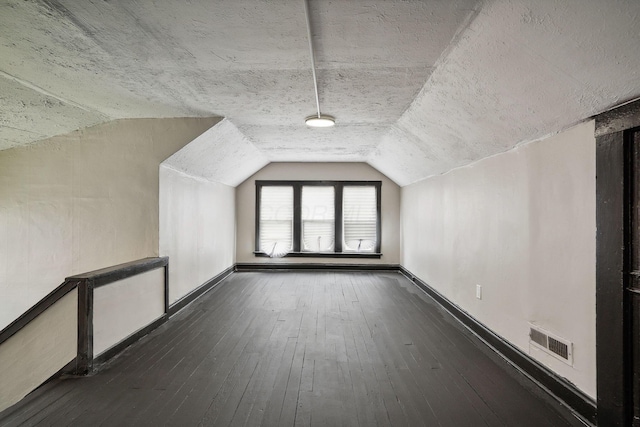 additional living space featuring visible vents, baseboards, dark wood-type flooring, and vaulted ceiling