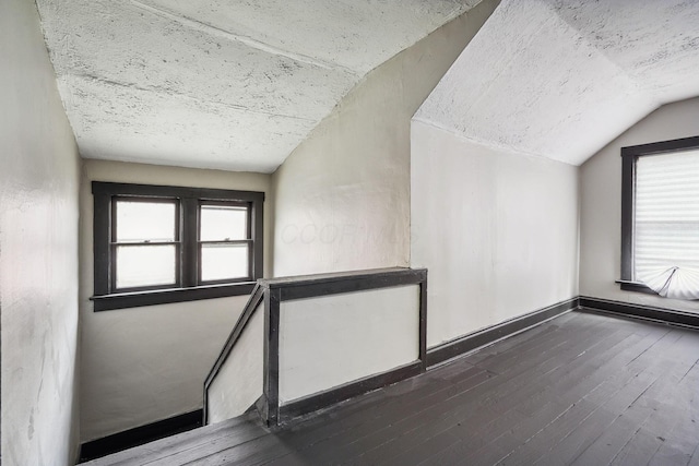 interior space featuring baseboards, lofted ceiling, dark wood-type flooring, and a textured ceiling