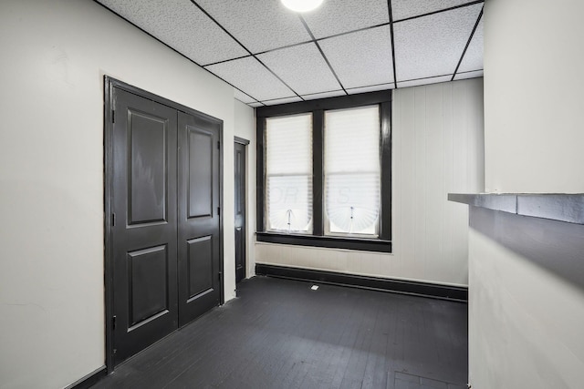 spare room with dark wood-style floors, a drop ceiling, and baseboards