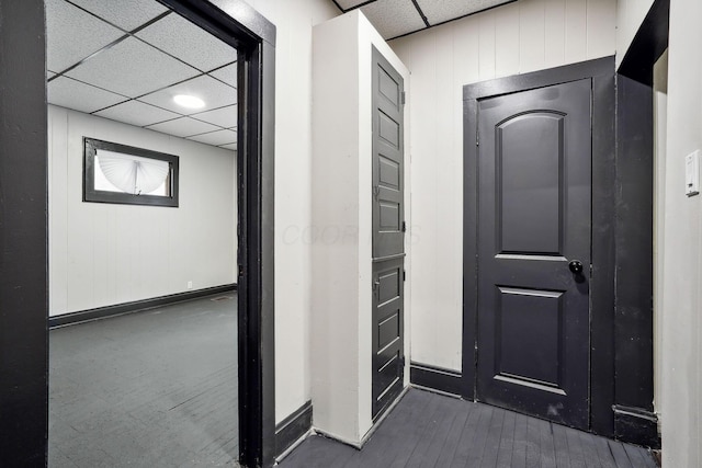 hallway featuring dark wood finished floors, a paneled ceiling, baseboards, and wood walls