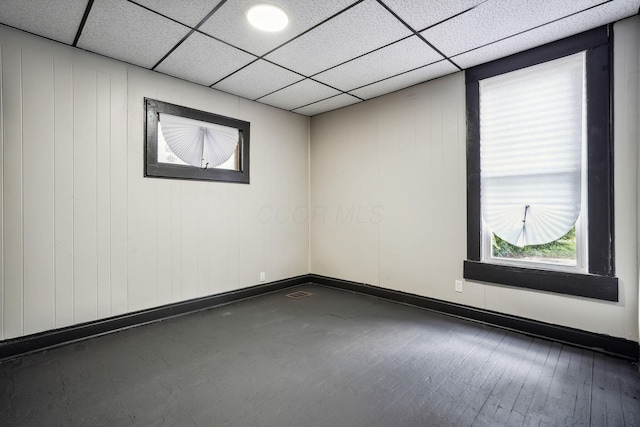 unfurnished room with a drop ceiling, baseboards, visible vents, and wood finished floors