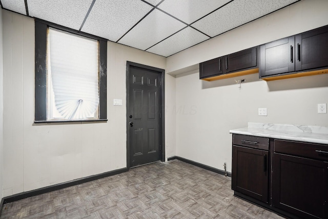 kitchen featuring baseboards, a paneled ceiling, and dark brown cabinets