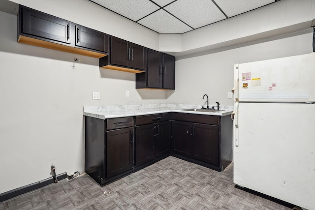 kitchen with a sink, freestanding refrigerator, light countertops, a paneled ceiling, and baseboards