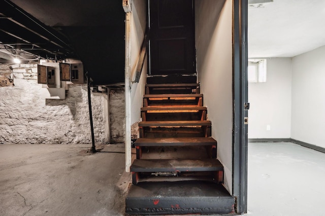 staircase featuring electric panel and concrete flooring