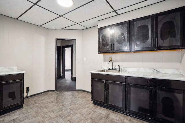 kitchen featuring parquet flooring, baseboards, a drop ceiling, and a sink