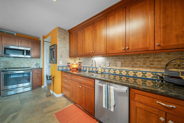 kitchen with brown cabinetry, dark stone countertops, stainless steel appliances, and a sink