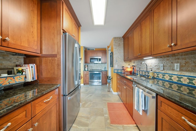 kitchen featuring backsplash, dark stone counters, brown cabinetry, stainless steel appliances, and a sink