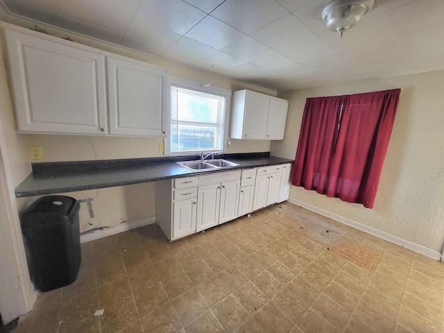 kitchen featuring white cabinetry, dark countertops, baseboards, and a sink