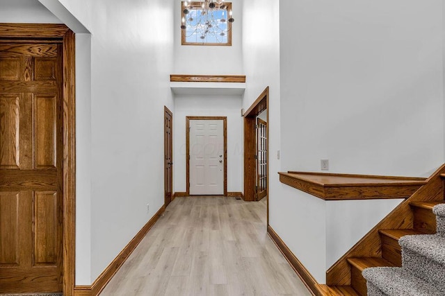 corridor featuring stairs, baseboards, light wood-type flooring, and a towering ceiling