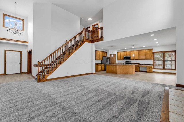 unfurnished living room with stairway, baseboards, a high ceiling, light carpet, and a notable chandelier