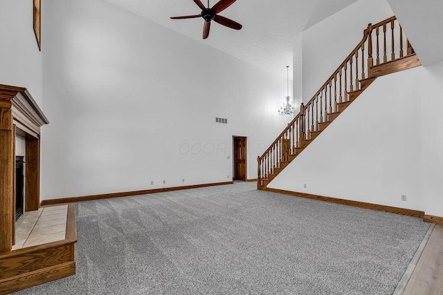 unfurnished living room with ceiling fan with notable chandelier, stairway, baseboards, and a high ceiling