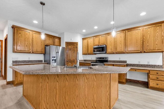 kitchen with a sink, appliances with stainless steel finishes, a center island with sink, and dark stone countertops