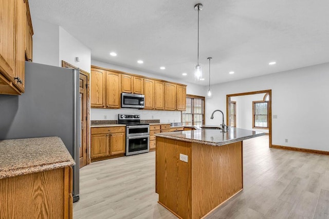 kitchen with light wood finished floors, appliances with stainless steel finishes, an island with sink, and a sink