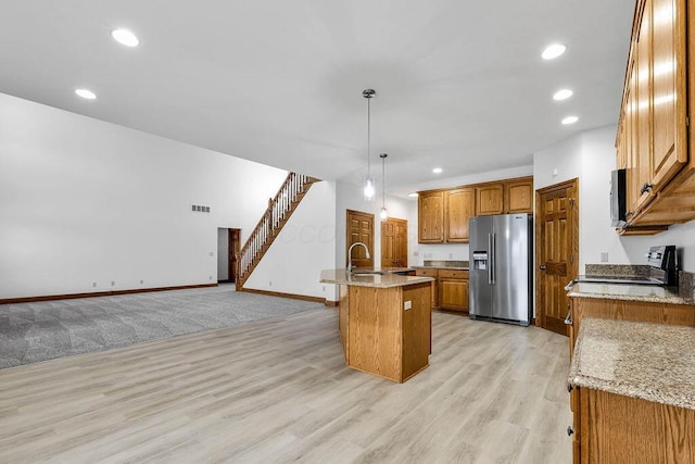 kitchen with a center island with sink, high end refrigerator, light wood-style flooring, recessed lighting, and brown cabinetry