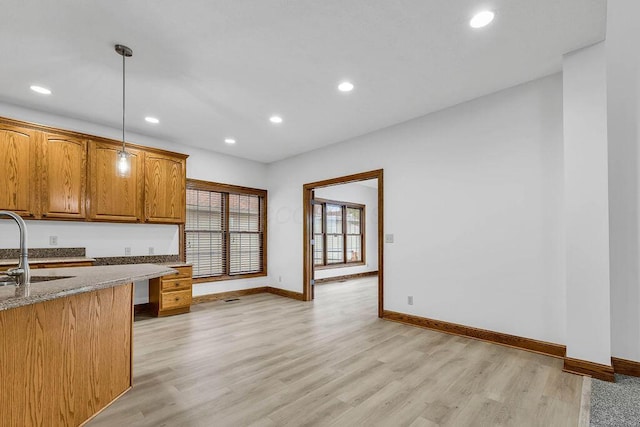 kitchen featuring a sink, baseboards, light stone countertops, and light wood-style flooring