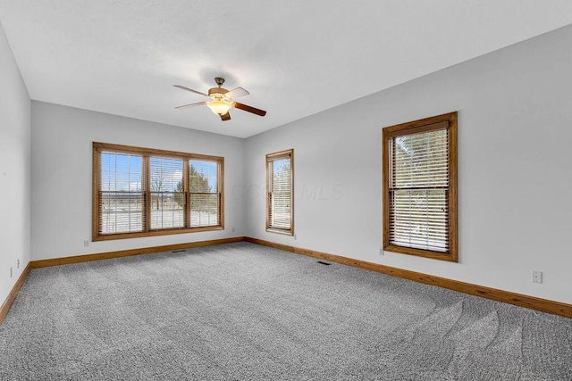 carpeted empty room with visible vents, a ceiling fan, and baseboards