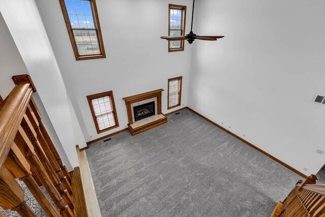 unfurnished living room featuring a tiled fireplace, carpet flooring, a ceiling fan, and baseboards