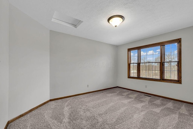 carpeted spare room featuring a textured ceiling, attic access, and baseboards