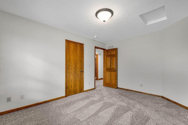 empty room featuring attic access, light colored carpet, baseboards, and a textured ceiling