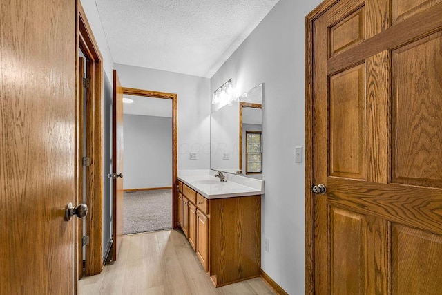 bathroom with a textured ceiling, vanity, baseboards, and wood finished floors