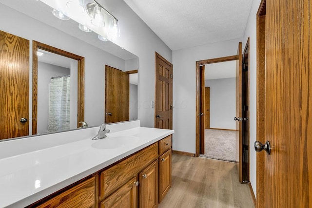 full bathroom featuring a textured ceiling, vanity, baseboards, and wood finished floors