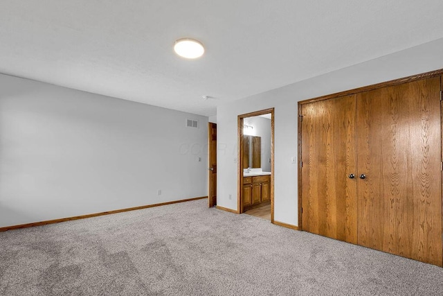 unfurnished bedroom featuring visible vents, light carpet, ensuite bath, a closet, and baseboards