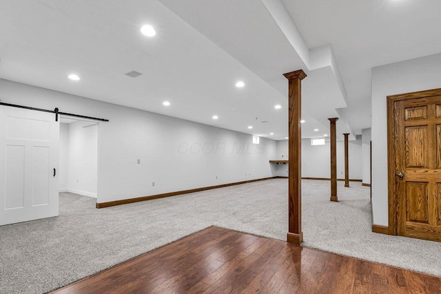 finished basement featuring a barn door, baseboards, visible vents, and wood finished floors