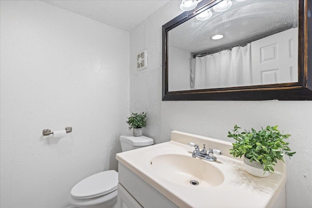 bathroom featuring a textured ceiling, toilet, vanity, and a textured wall